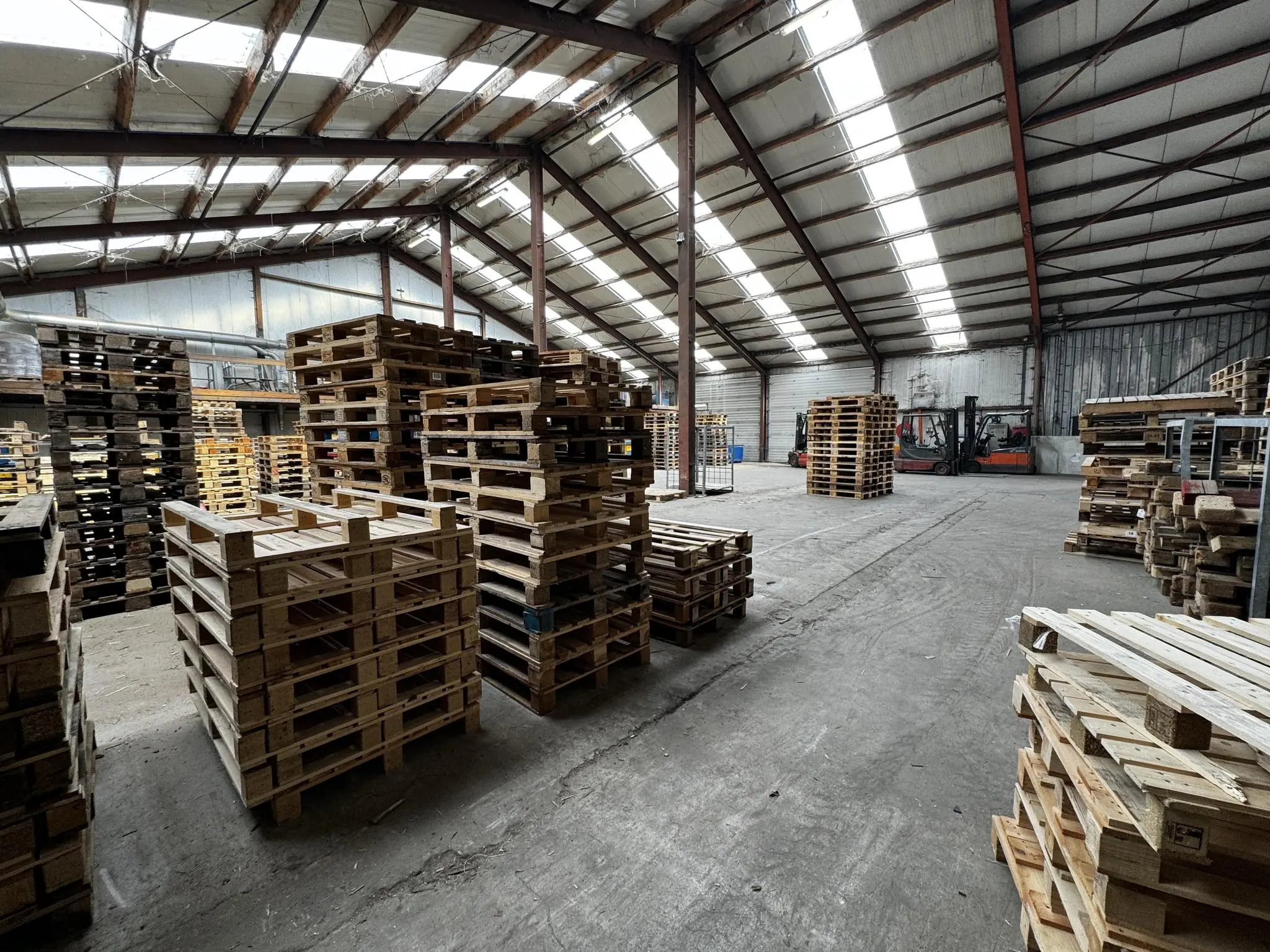 Binnenzicht van een loods aan de Graaf van Lynden van Sandenburgweg met stapels houten pallets en heftrucks op de achtergrond.